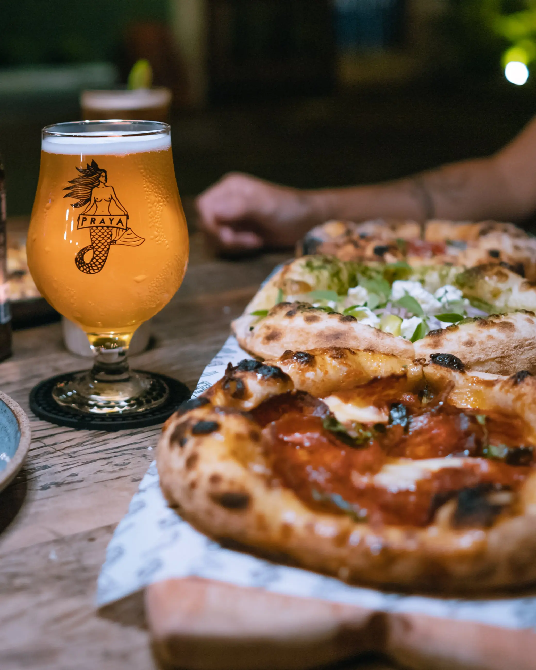 Duas pizzas recém-saídas do forno e um chope gelado na mesa de madeira, à noite.