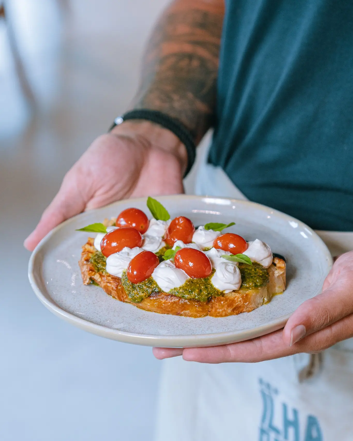 Prato servido à mão pela equipe: fatia de pão tostado com pesto, burrata, tomate-cereja e manjericão.