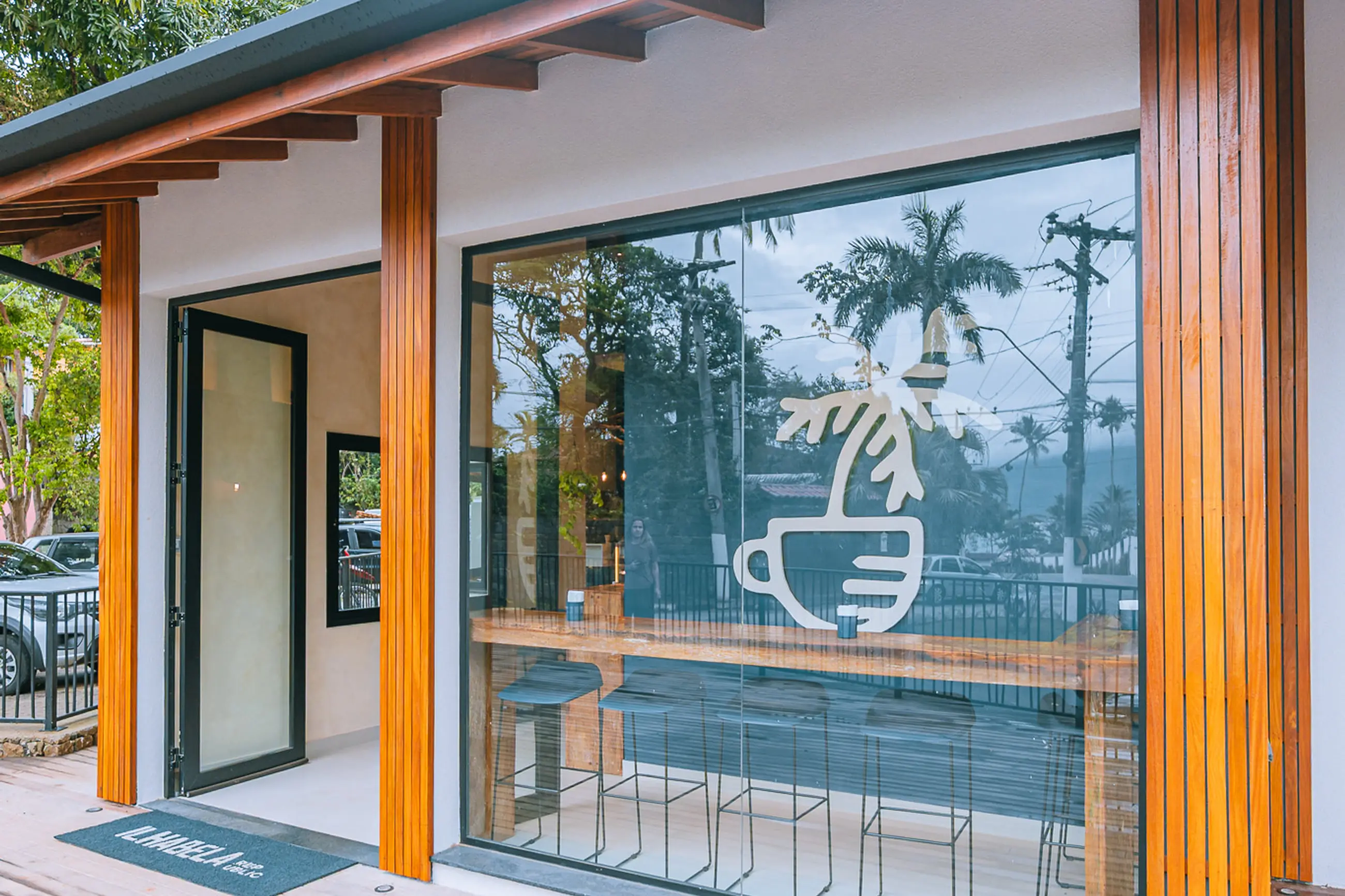 Fachada da Villa Porto com as portas sanfonadas abertas para o deck e o símbolo do coqueiro aplicado na vidraça.