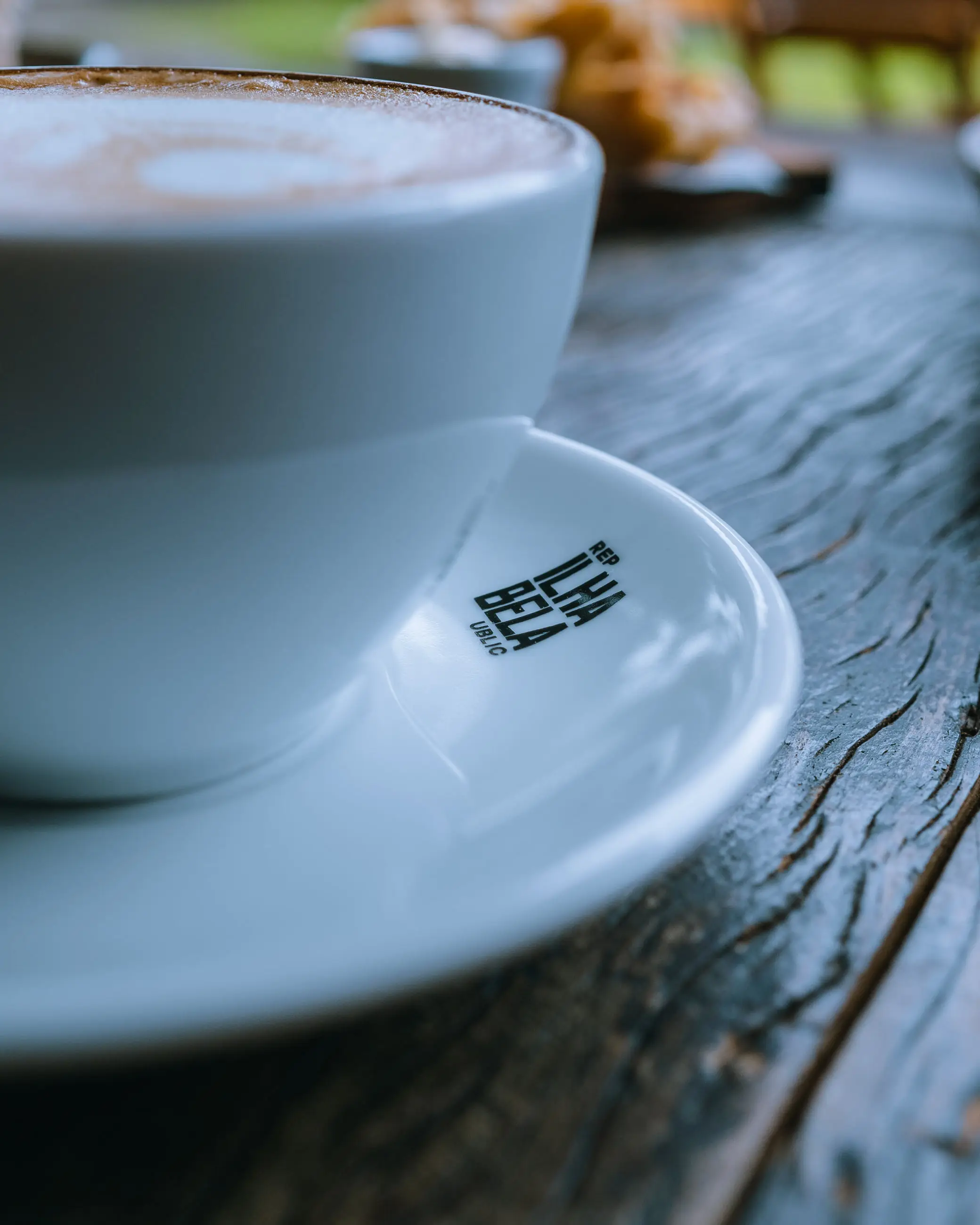 Cappuccino servido na xícara branca da casa, com o símbolo da Ilhabela Republic no pires.