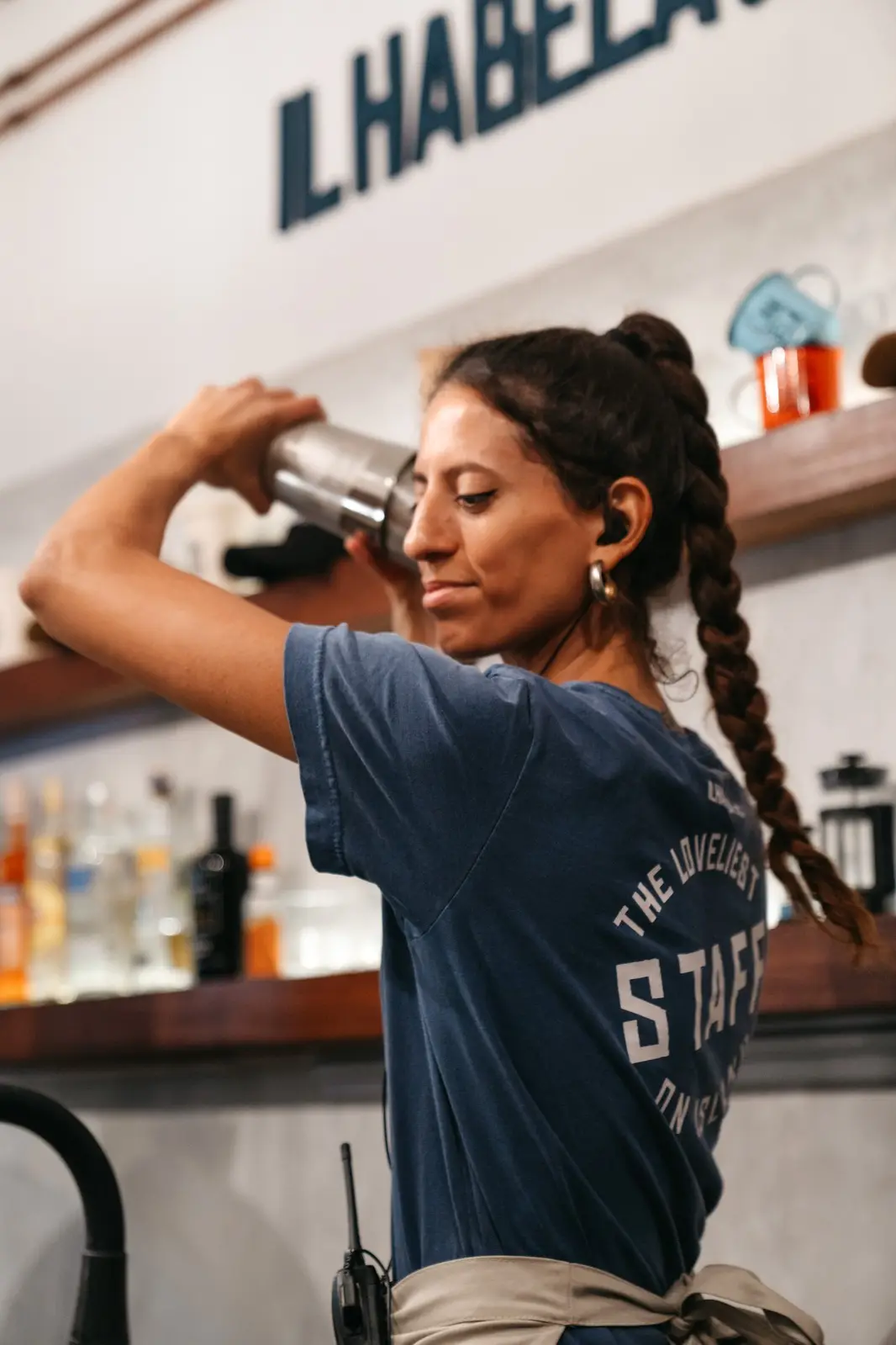 Bartender preparando um drink na coqueteleira, atrás do balcão.