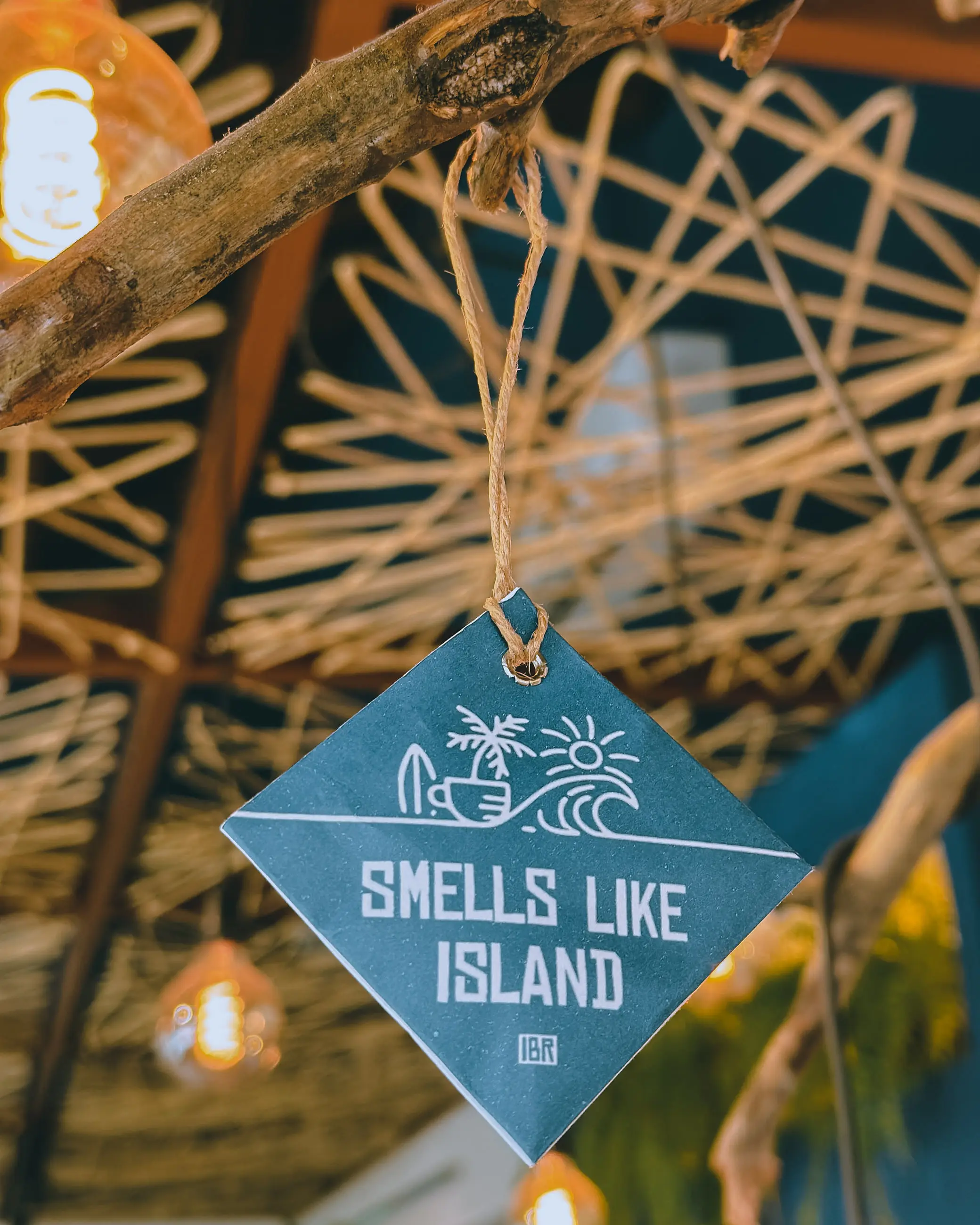 Aromatizador de papel Smells Like Island da Ilhabela Republic pendurado por um cordão de juta em um galho, dentro da casa.