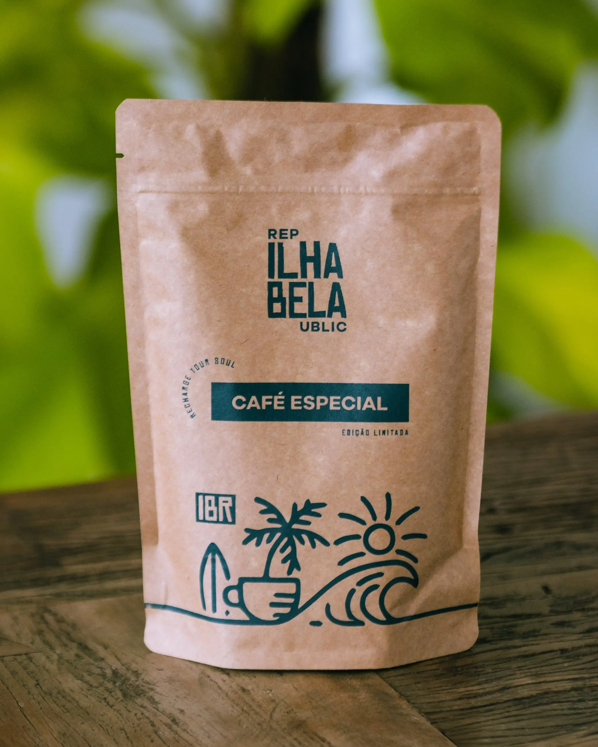 Pacote kraft de café especial da Ilhabela Republic sobre mesa de madeira, com folhagem verde desfocada ao fundo.